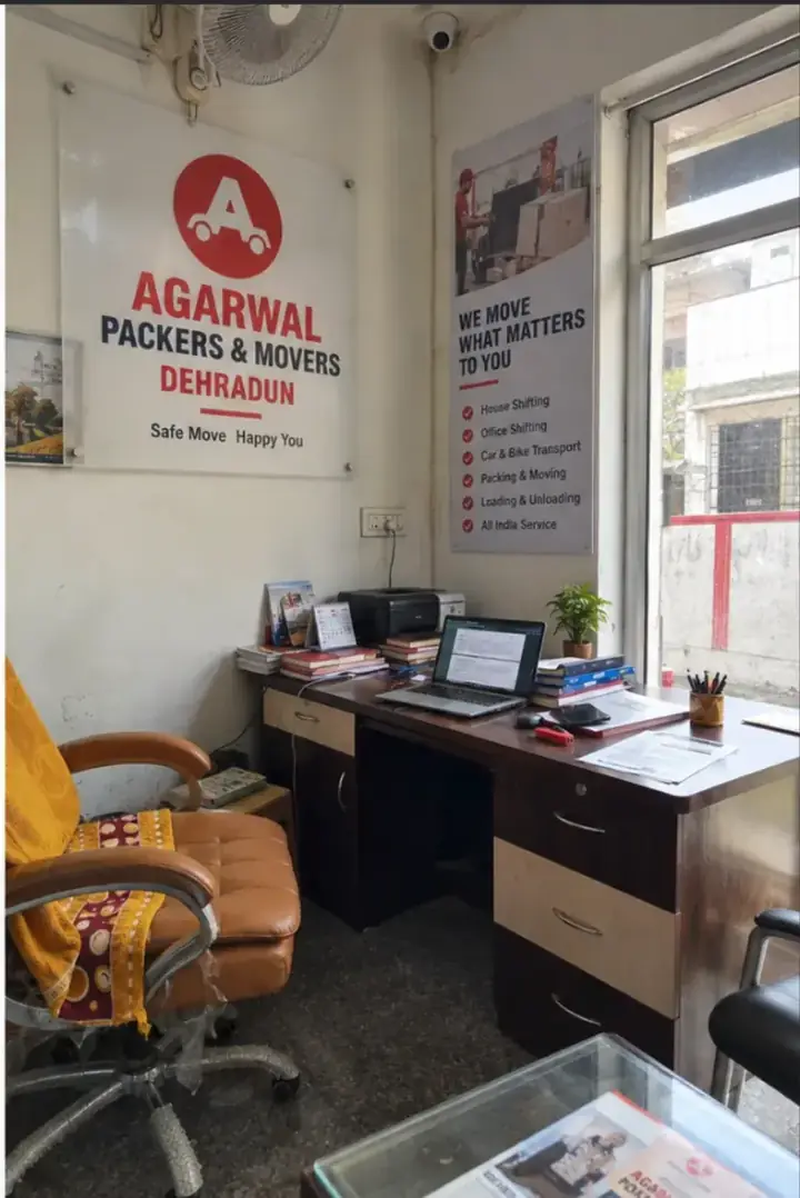 Inside the Agarwal Packers and Movers office in Dehradun, with the company logo on the wall and a service list board
