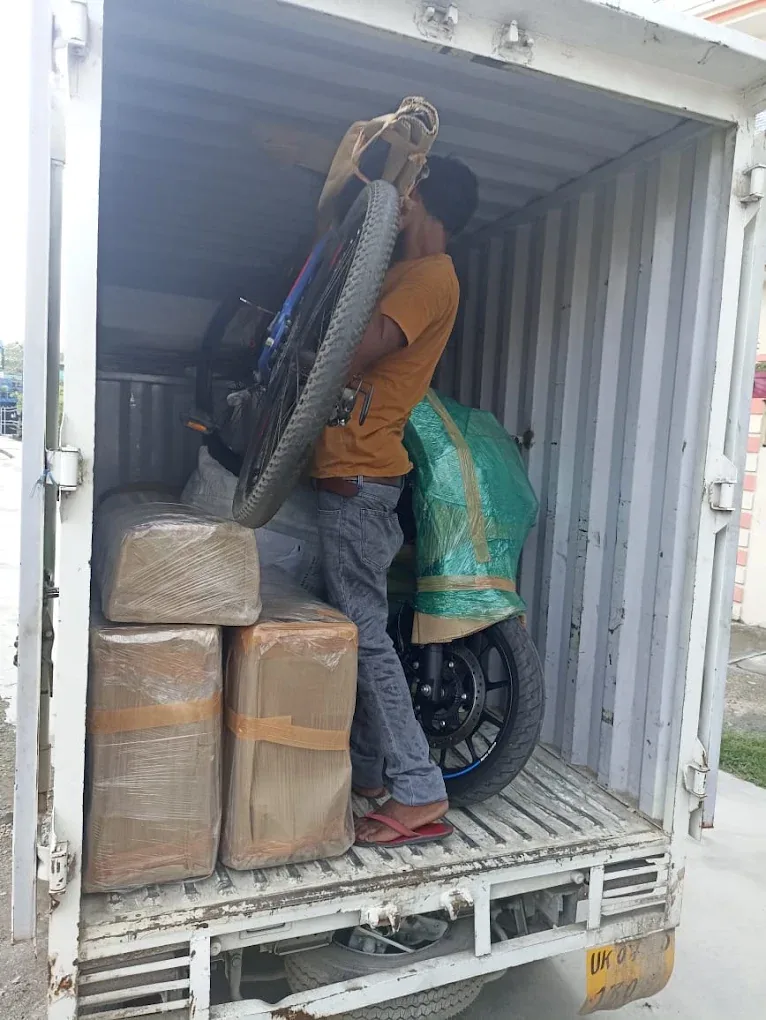 Agarwal Packers and Movers worker loading sealed cartons and a wrapped two-wheeler into a transport truck in Dehradun