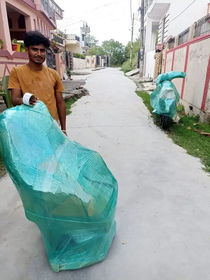Agarwal Packers and Movers crew member with a scooter and chair wrapped in stretch film in a Dehradun lane